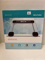 Front of the box showing the Beautural digital bathroom scale with glass platform, metal rods, black corner pads, and digital display.
