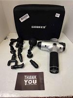Full view of the Gobees massage gun, all 10 interchangeable massage heads arranged in front, and the branded black carrying case behind them.