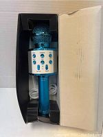 Blue handheld karaoke microphone in original packaging with built-in control panel and white USB charging cable.