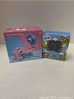 Two boxed items, a pink and blue kids digital camera and a smart watch in a cartoon-themed box.