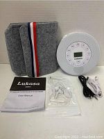 Full lot including Lukasa SN004 music player, grey felt carrying case with striped strap, user manual, white earphones in sealed bag, all arranged neatly on a white background.