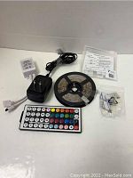 Full lot showing LED strip light roll, power adapter, remote control, audio sensor, and mounting hardware on a white surface.