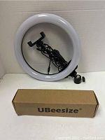 Photo of UBeeSize ring light with attached phone holder and tripod stand, alongside a branded box.