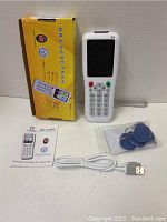 Photo of the ZX Copy RFID NFC card copier reader writer duplicator handheld device, its retail box, user manual, USB cable, and blue RFID key fobs on a white surface.