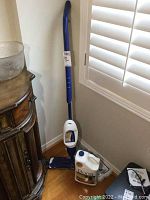 Full Bona mop system including mop, cleaner solution, and mop pads arranged on hardwood floor near window and furniture.