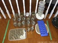 Photo of a group of various sized canning jars arranged on a wooden surface with small spice jars, plastic storage containers, and an ice cube tray.