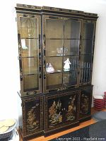 Front view of the large black painted Asian-style China cabinet showing glass doors with shelves and detailed gold and colored bird and floral decorations on both upper and lower sections.