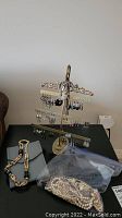 Metal earring stand holding over 20 pairs of earrings, some dangling with beads, with a bracelet and necklace displayed alongside in a plastic bag