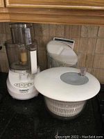 Cuisinart PowerPrep Plus food processor next to white salad spinner on countertop, showing the processor's buttons and clear bowl.
