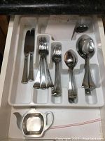 Photo of cutlery set arranged in white plastic tray showing knives, salad forks, dessert forks, teaspoons, soup spoons and a grapefruit spoon.