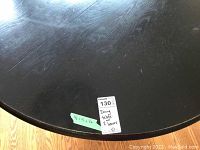 Close-up view of the round dark wood table top showing wear marks and scratches. Includes green sticker with table dimensions 46x46x30.