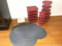 Photo showing the collection of glass storage containers stacked in two piles and 10 dark gray oval placemats spread out in front.