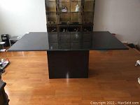 Full view of rectangular black granite tabletop on pedestal base in room setting