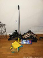 Assorted wood, plastic, and fabric furniture hangers, window squeegee, and packaged Vileda mop head displayed on hardwood floor.