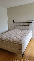 Photo showing metal headboard with decorative scrollwork and vertical bars, fitted to a disassembled bed frame without mattress or box spring.