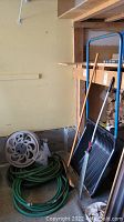 Photo showing all items including garden hoses coiled on the floor, tools leaning against a shelf, and the manual hose reel.
