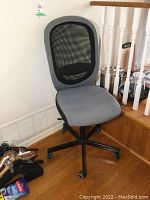 Full view of the IKEA office chair showing gray fabric seat, mesh backrest, adjustable height base with caster wheels.