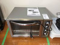 Front view of KitchenAid stainless steel countertop oven with glass door, chrome handle, and instruction manual on top.