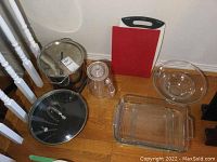 Collection of kitchenware including glass baking dishes, mixing bowls, cutting boards, metal cooking pot with lid and fry pan with lid.