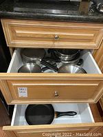 Drawer open showing four stainless steel pots with handles and lids inside a wooden drawer.