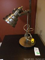 Metal table lamp with swivel bell-shaped head, cylindrical stand, round base, and power cord with yellow switch wrapped around stand.