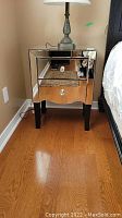 Front view of one mirrored side table with a lamp on top, showing overall appearance and condition