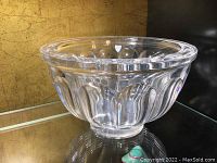 Clear heavy glass bowl with vertically ribbed fluted pattern and thick rim on reflective surface.