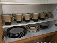 Shelf with the mugs and cream and sugar set on top; bowls and plates underneath