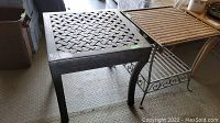 Metal outdoor side table with dark woven metal lattice top surface beside second metal side table with woven wicker top and metal scroll frame