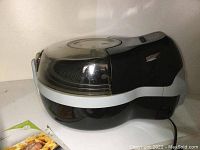 Front and side view of T-fal ActiFry 2-in-1 air fryer with clear lid and instruction manual and recipe book copies on counter.