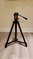 Photo showing the full aluminum tripod standing on a wood floor, ready to use with the pan/tilt head and adjustment handle visible.