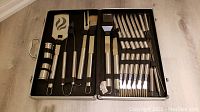 Full view of open aluminum carrying case showing all 24 pieces of barbecue and steak knife set arranged inside foam lining.