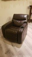 Front view of brown child's leather recliner chair, showing padded seat, back, armrests, and cup holder on right armrest.