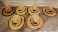 Photo showing six brand new Corona straw cowboy hats in various beige and tan shades with Corona logo patch on front.