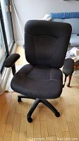 Front view of grey fabric office executive chair showing padded seat, armrests, and base with caster wheels. Chair in good condition with minor staining visible.
