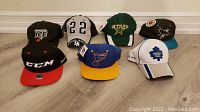 Photo showing seven brand new hockey hats arranged on floor with clear view of logos and colors.