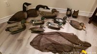 Full view of the 11 duck and goose hunting decoys arranged on floor with carrying bag in front