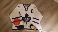 Front view of white Toronto Maple Leafs hockey jersey with Mats Sundin number 13 and captain's C patch, stored in plexiglass.