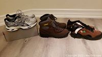 Photo showing three pairs of shoes: ASICS runners, brown winter boots, brown and black steel toe shoes all brand new.