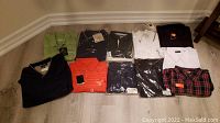All shirts laid out on floor showing full lot with tags, various colors and styles