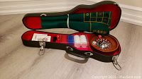 Open case showing miniature roulette wheel, felt betting cloth, plastic chips, dice, and instruction manual inside.