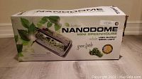 Closed box of Nanodome Mini Greenhouse showing branding, product image and grow light mention.