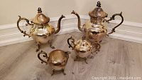 Photo showing full tea set of two teapots, sugar bowl, creamer with ornate handles and feet