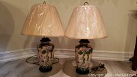 Photo of pair of vintage ceramic table lamps with beige pleated lampshades, plastic wrapped, sitting on wooden floor, cords visible.