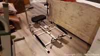 Side view of vintage rowing machine showing padded seat, footrests, frame, and resistance handles.