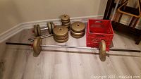 Wide view showing bench press barbell with weight plates on the floor along with dumbbell bars and a red crate.