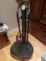 Front view of black whole body vibration machine with control panel and resistance bands.