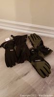 Photo showing two pairs of winter gloves on the floor, one black branded HEAD, the other olive green and black branded POWERSTAR, both size medium and brand new.