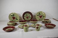 Full set display showing all 15 items, including large bowls, plates, cups, saucers, and salt & pepper shakers with hand-painted floral design in red, green, beige and maroon.