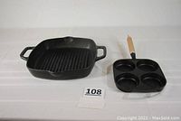 Photo showing two cast-iron pans on white surface, muffin pan with wooden handle on right and square grill pan with dual handles on left.